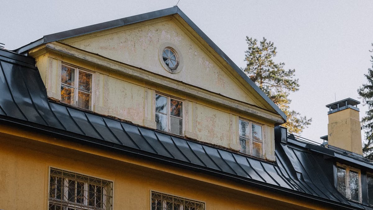 Close-up of a vintage house with a rustic yellow facade and black metal roof in an autumn setting.